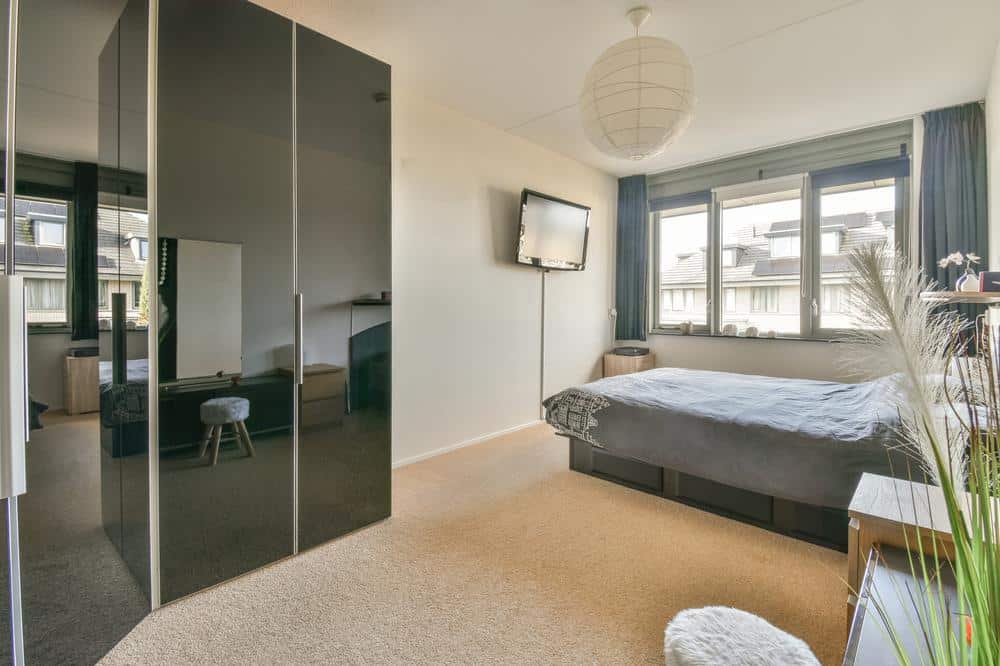 Windowed bedroom with black door closet and grey sheet bed