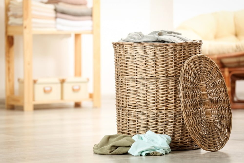 A cloth basket full of clothes on the floor of a room