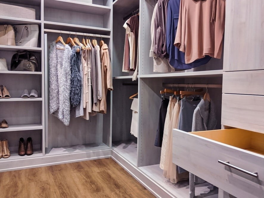 Grey colored walk in closet full of clothes with wooden flooring