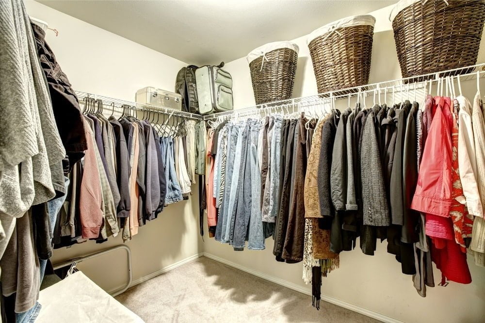 A walk-in closet with hanging racks and hanged clothes that has three baskets top of them