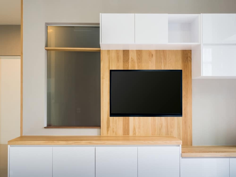 A medium sized tv mounted on open designed tv cabinet with small white cabinets