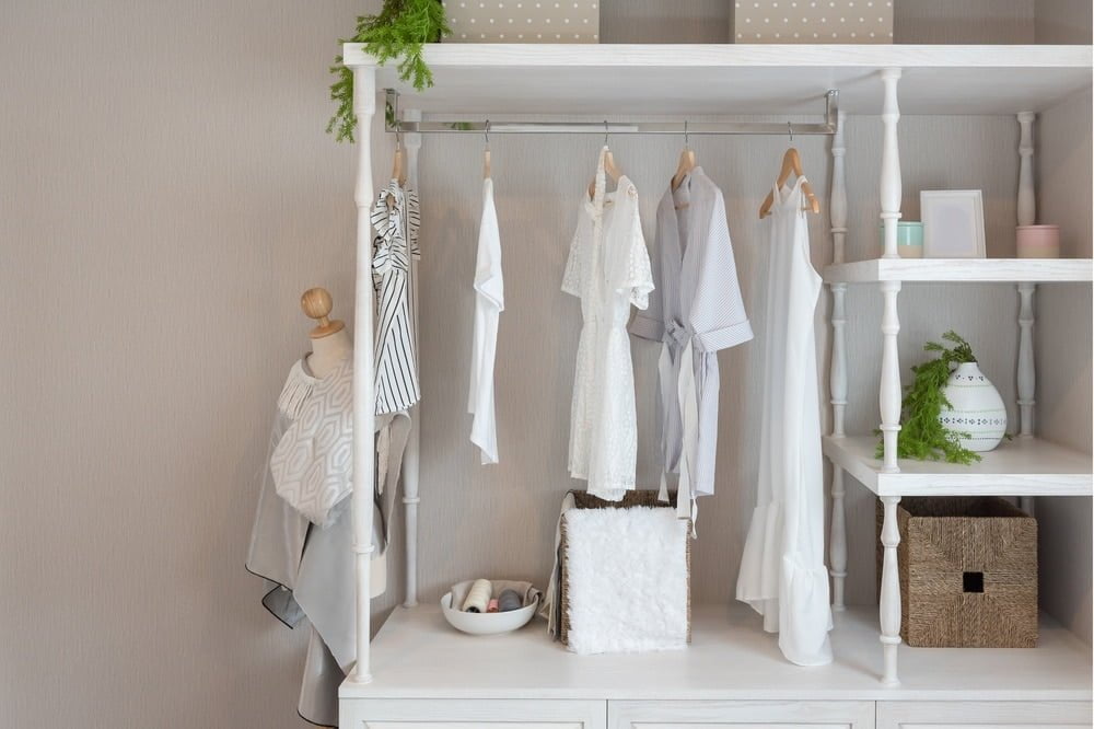 Small white open closet has white clothes hanging