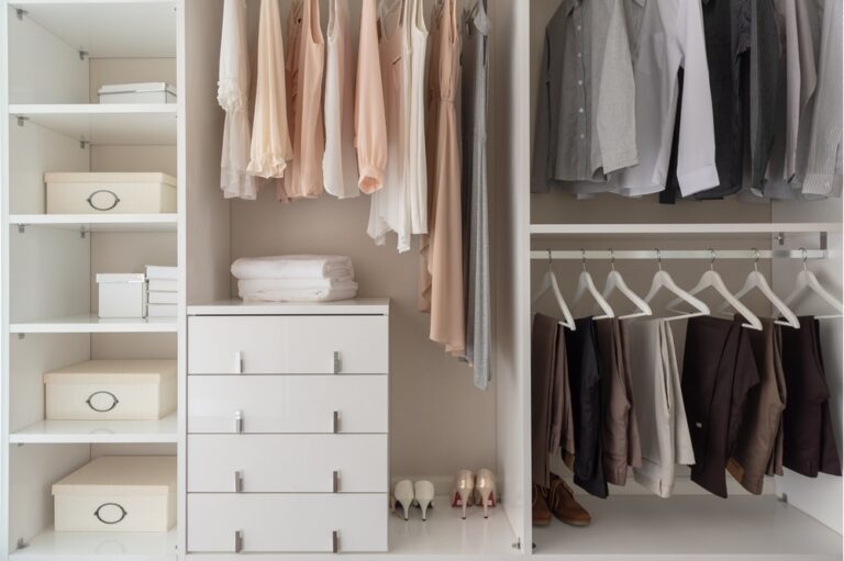 Interior of an white open closet with drawers and clothes hanging inside