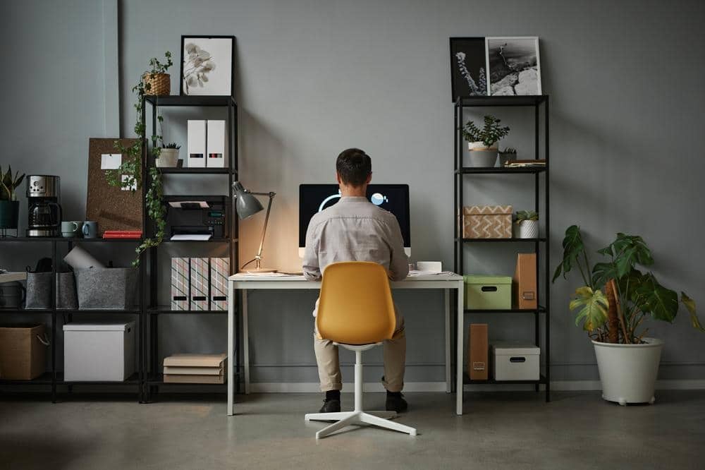 a person sitting on a chair next to a desk between shelves