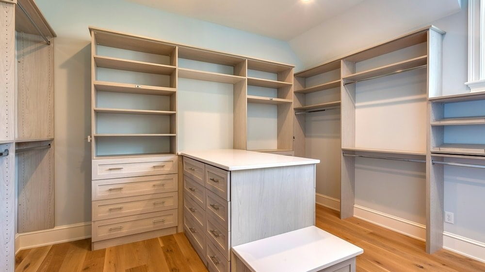 Empty wooden walk-in closet with island next a small bench