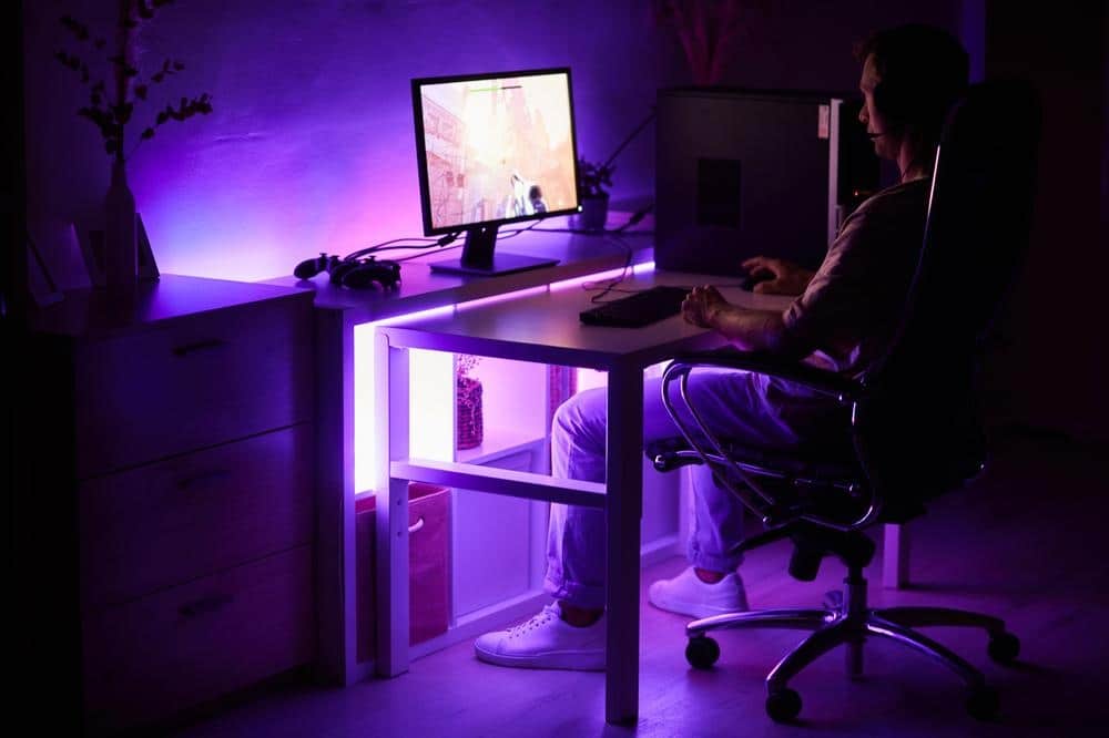 Dark room with led lighted desk with a pc and a person sitting next to it