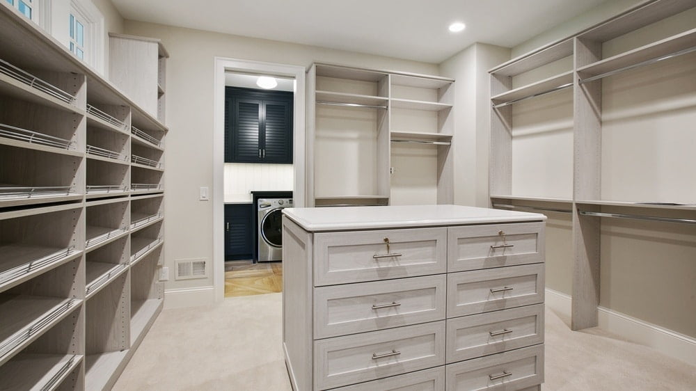 Empty white walk-in closet with white island drawers