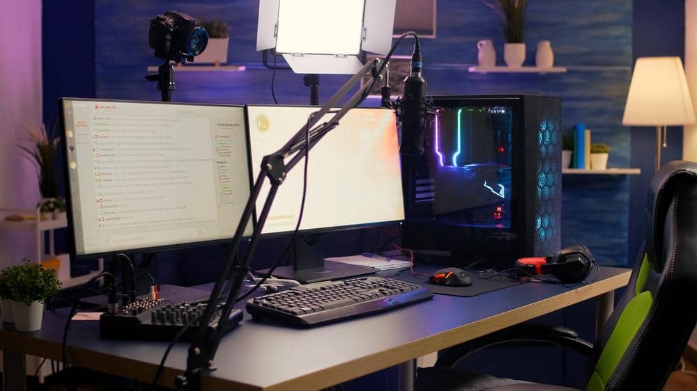 A desk with two monitors and pc case and a microphone in a room