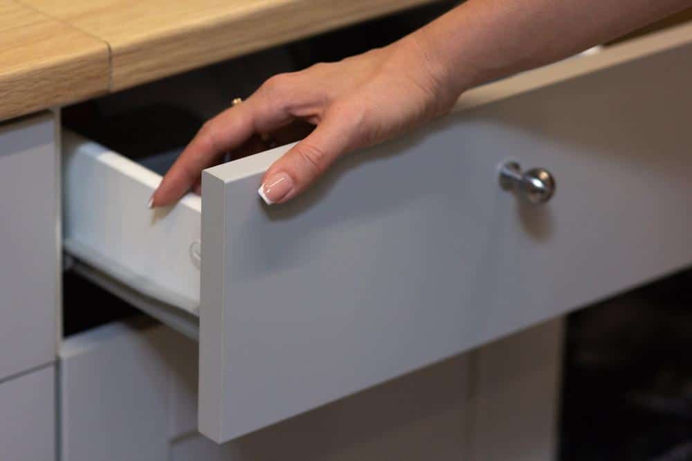 A grey drawer under wooden counter opened by a persons hand