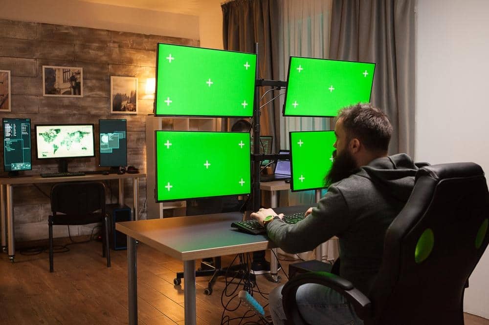 A man sitting in front of four monitor pc in a room