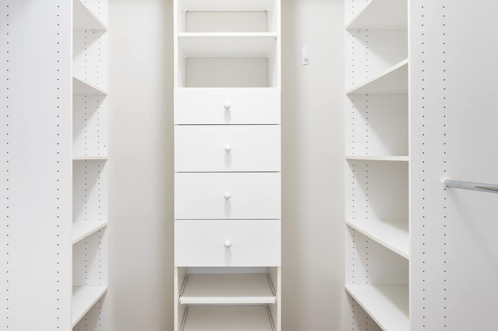 Empty white narrow walk in closet with drawers and shelves
