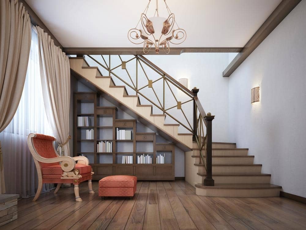 A built in bookcase under stairway in a room with red armchair and ottoman