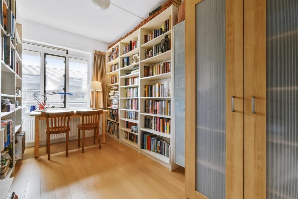 Wooden floor home library with wall covered bookcase and glass door closet