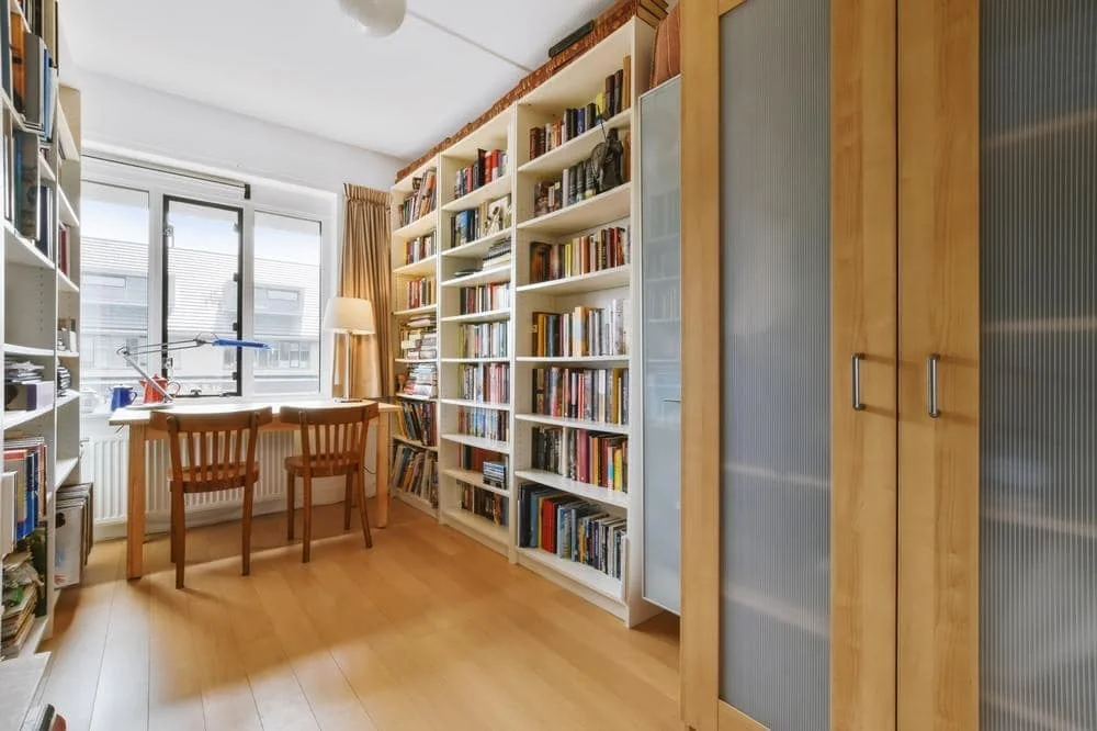 Wooden floor home library with wall covered bookcase and glass door closet