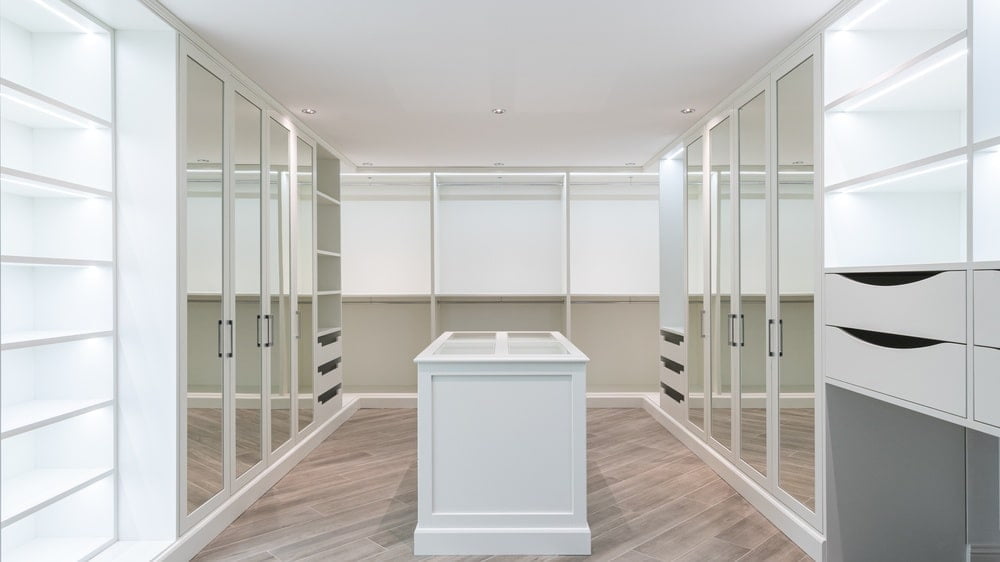 White walk in closet with mirror door cabinets and white island in the midde