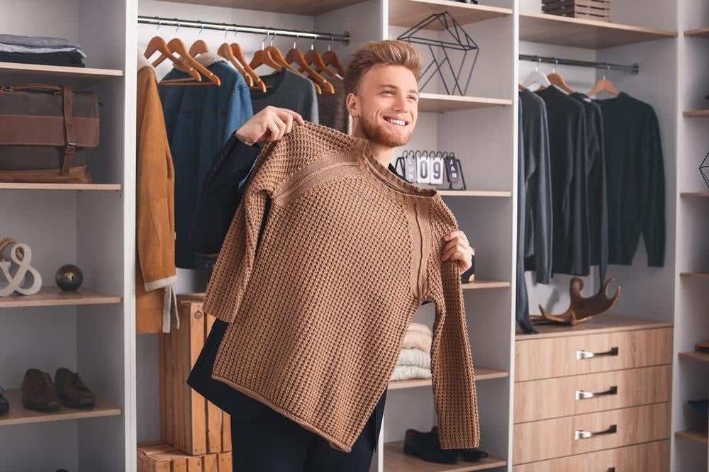 A man holding a clothing in front of a custom closet