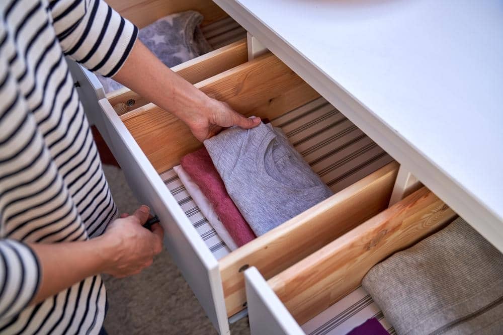 Man reaching a folded clothing in a opened drawer