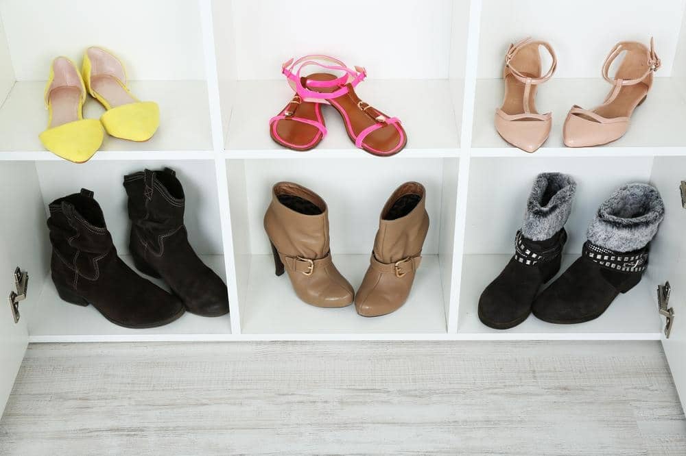 Different types of shoes inside of a sectioned white closet with open doors