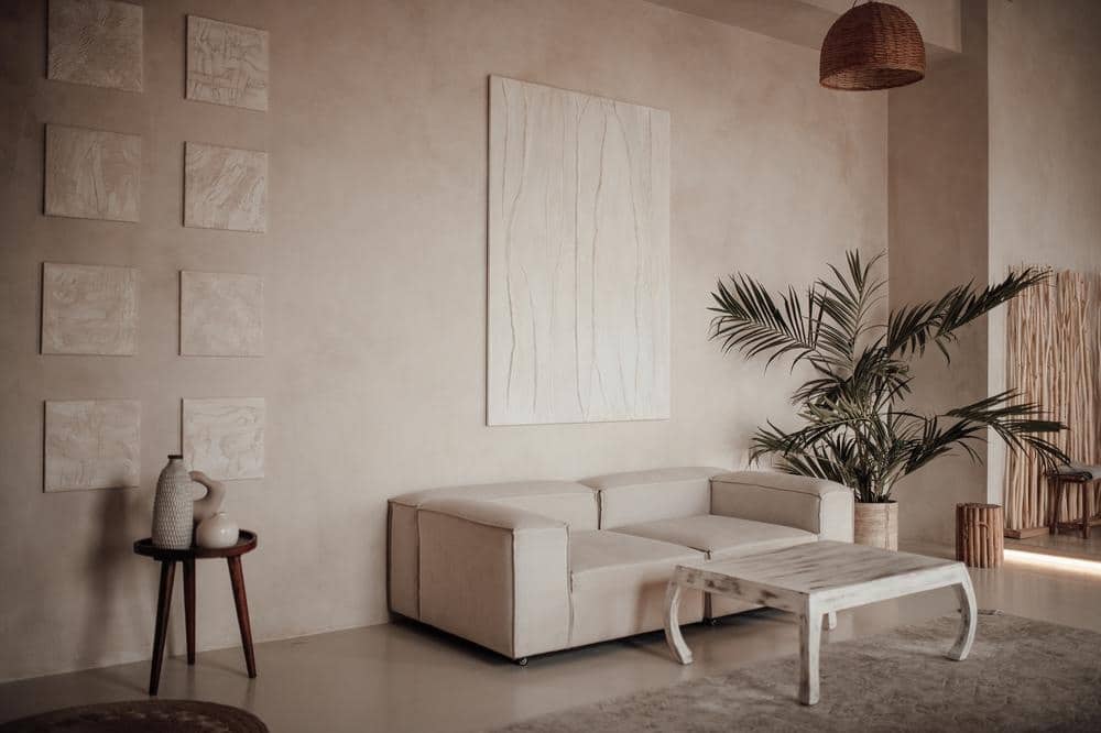 Small room with beige walls with artwork on it and couch next to a plant