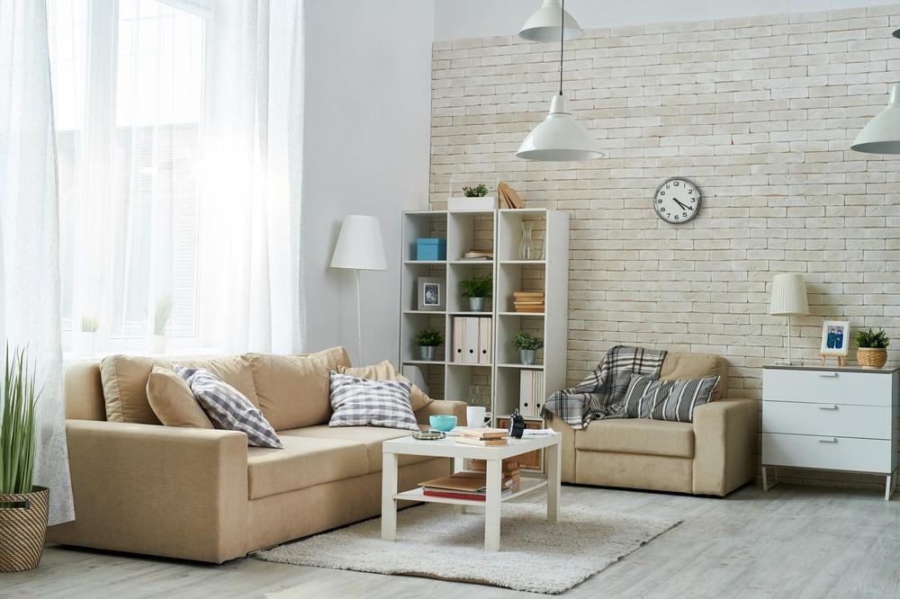 Corner of a living room that has white bookcase and beige couches with white wooden coffee table