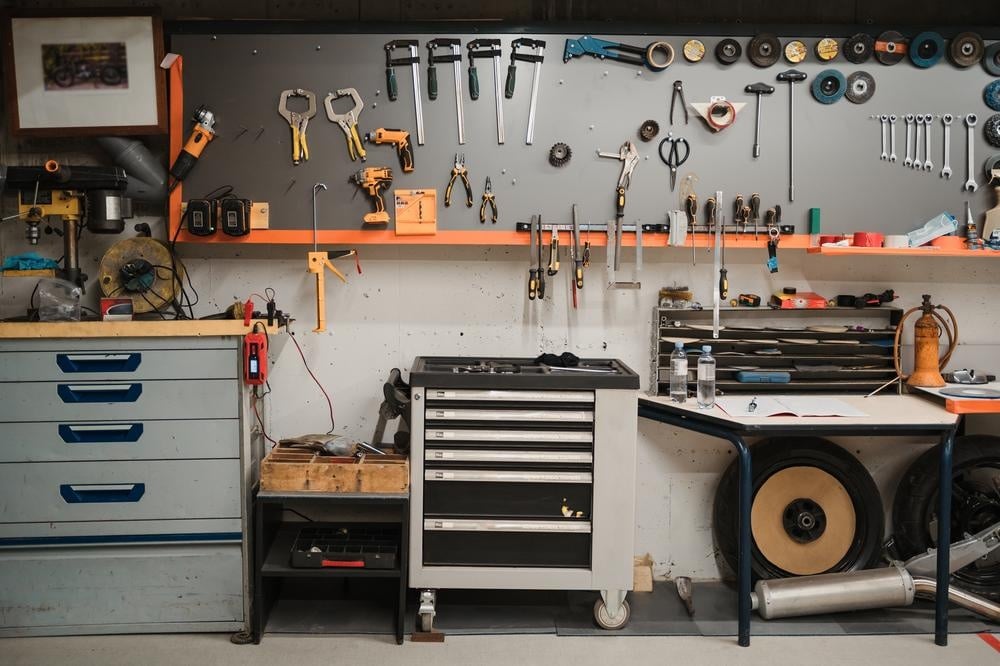 Unorganized garage with tools on the wall and storage containers on the floor