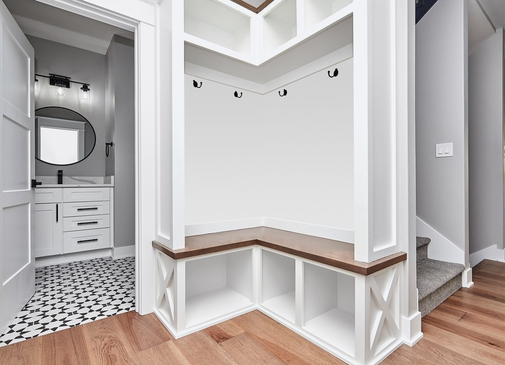 White mudroom with dark wooden bench and storage sections above