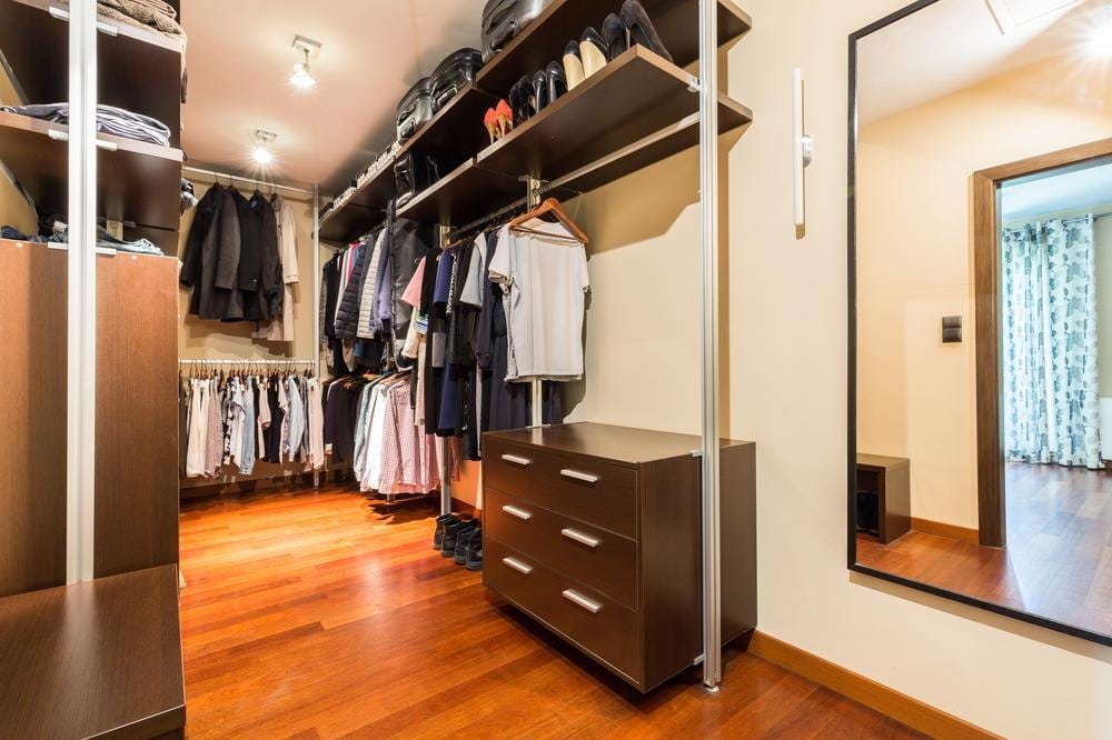 Small walk in closet with open shelves and drawers next to a mirror on the wall