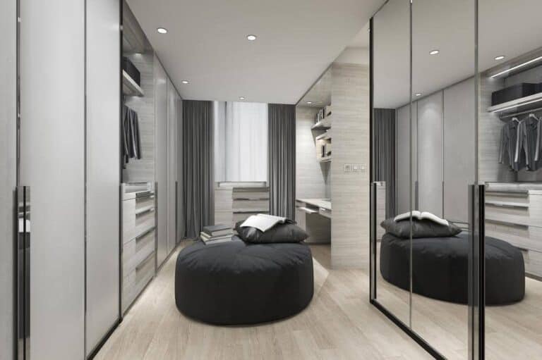 Large walk in closet with mirrored door closets and a black ottoman in the middle