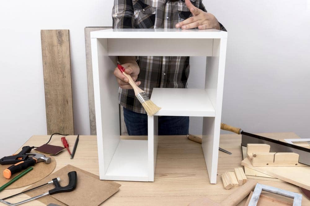 A person painting a white closet part on a wooden table