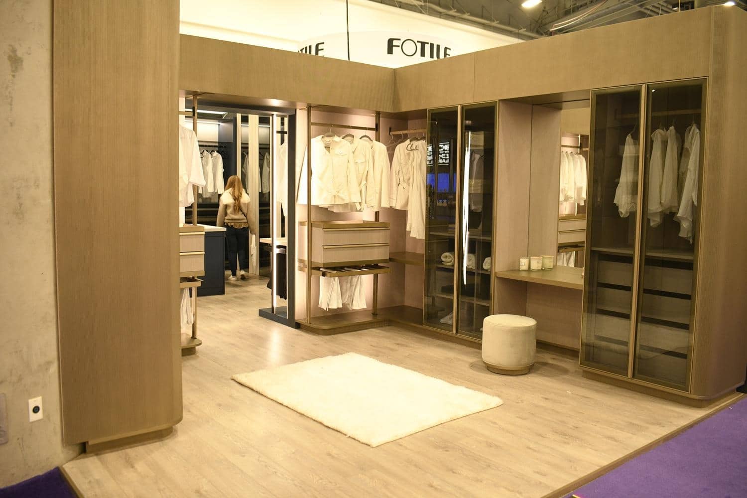 A walk in closet with light wooden finishes and a white rug on the floor
