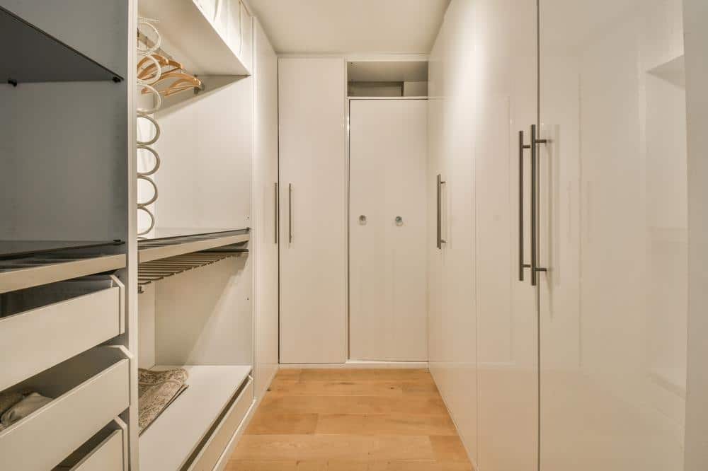 White narrow walk in closet with empty hangers and shelves