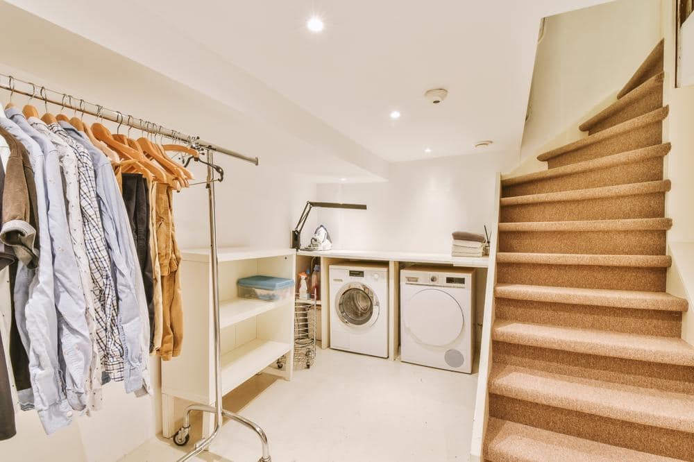 Light beige laundry room with stairs and clothing hangers