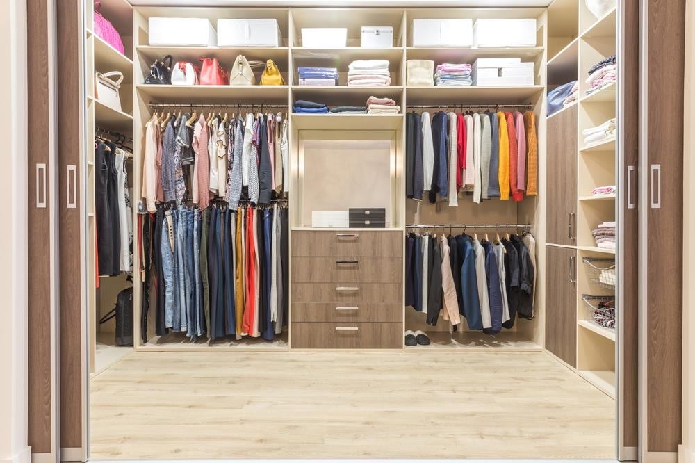 Organized walk in closet with hanging clothes and closed drawers made of wood