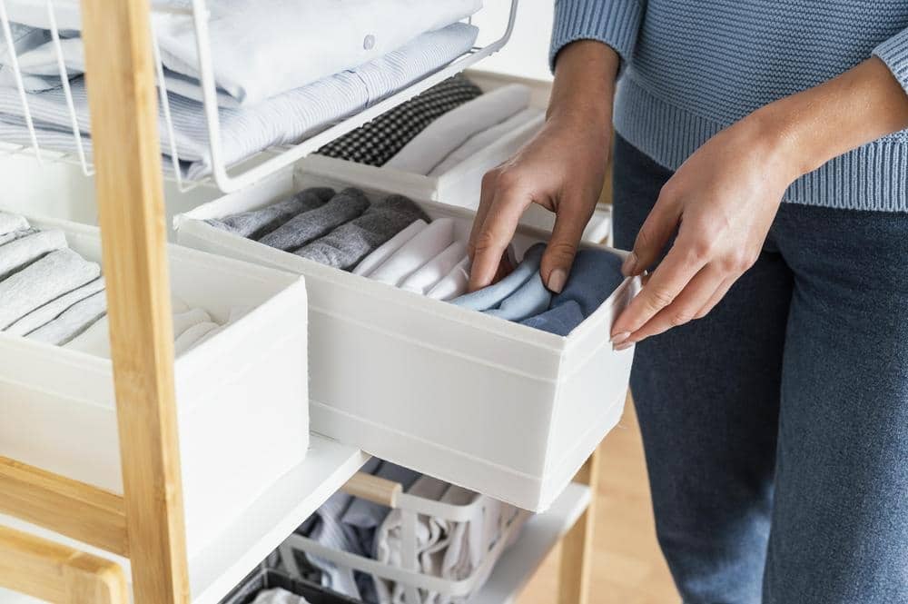 A person putting folded clothes inside of a fabric drawer