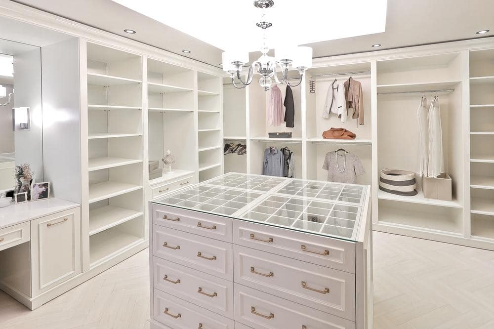 White large walk in closet with a lot of empty shelf and a island with drawers and glass countertop