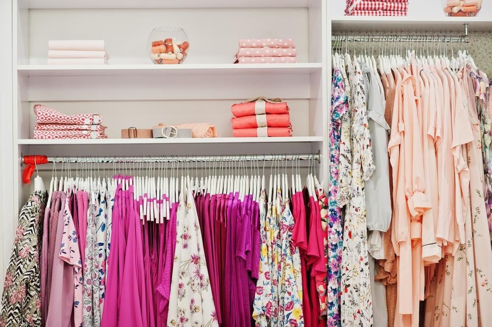 Pink clothes hanging on a white closet with large shelves that has accessories