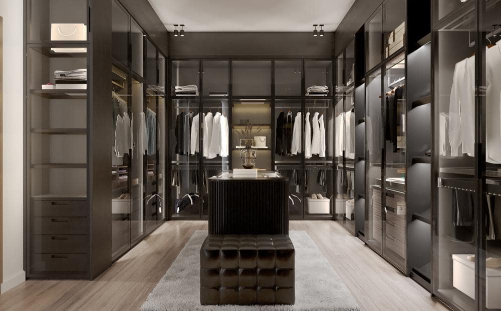 Modern black walk in closet with lighting, glass doors and dark island in the middle