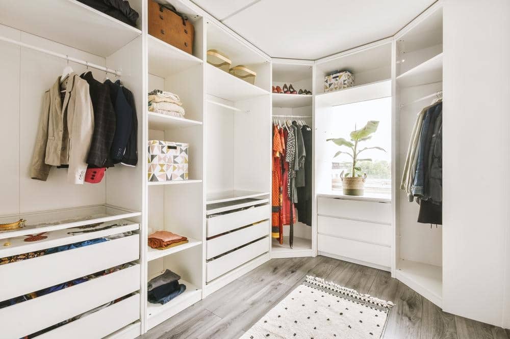 White walk in closet with a window and open sectioned shelves with racks and a plant