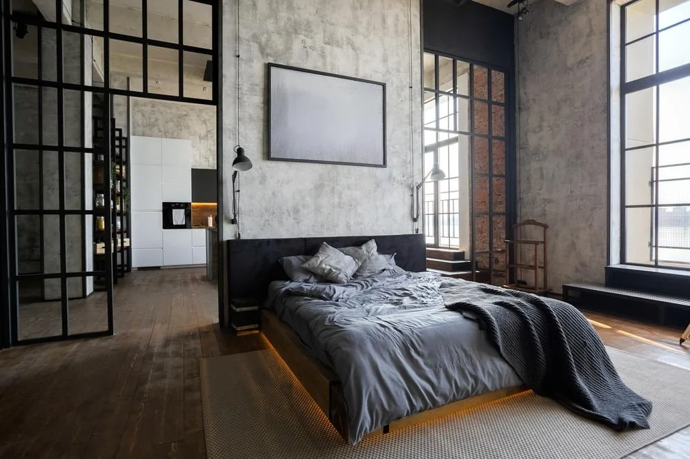Large modern industrial style bedroom with large windows and dark sheeted bed
