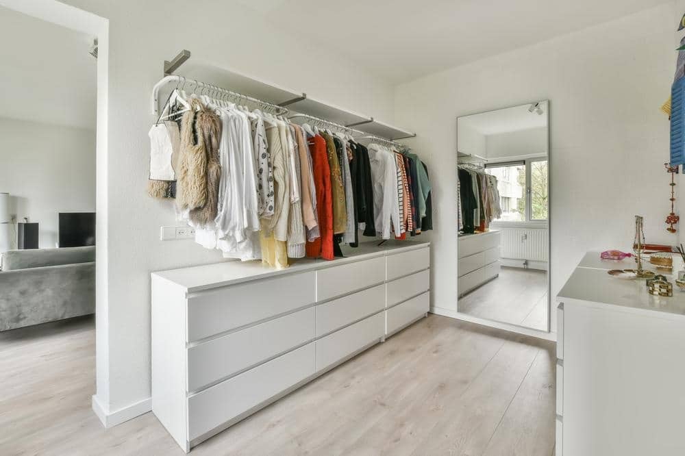 White room with a mirror and large drawers and hanging rods above them