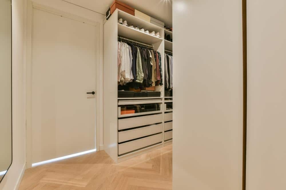 White closet walk in closet with drawers and hanging rods full of clothes