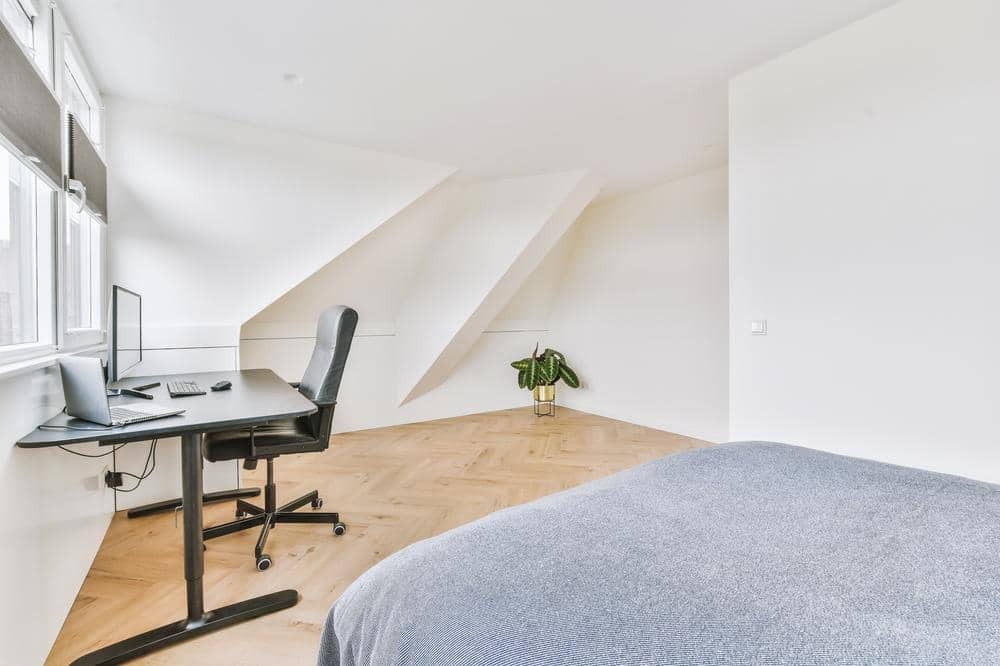 Spacious attic room with white walls and working desk and a bed