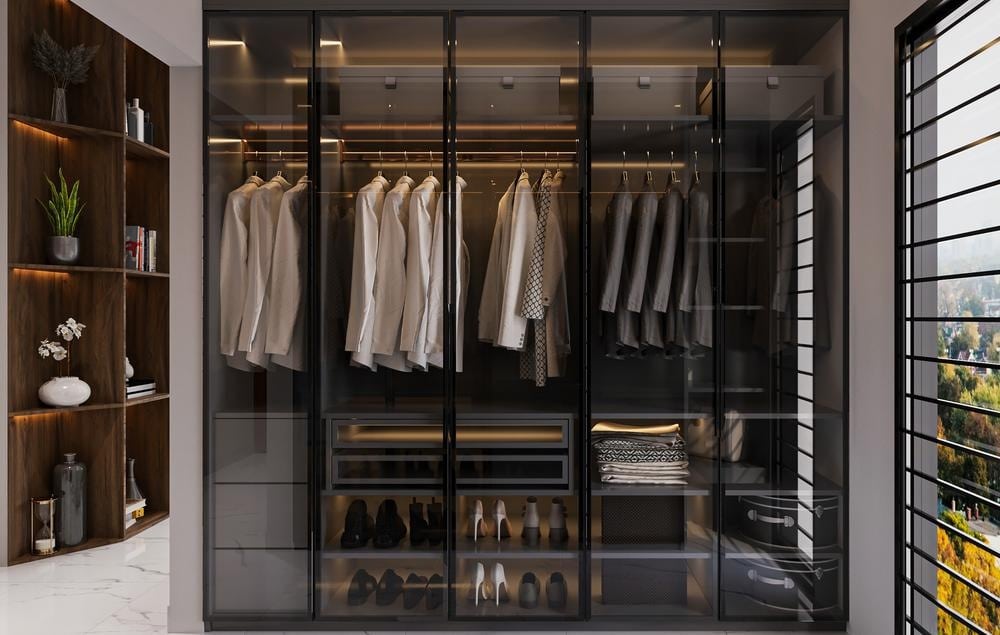 Modern custom closet with glass doors and there are hanging shirts inside