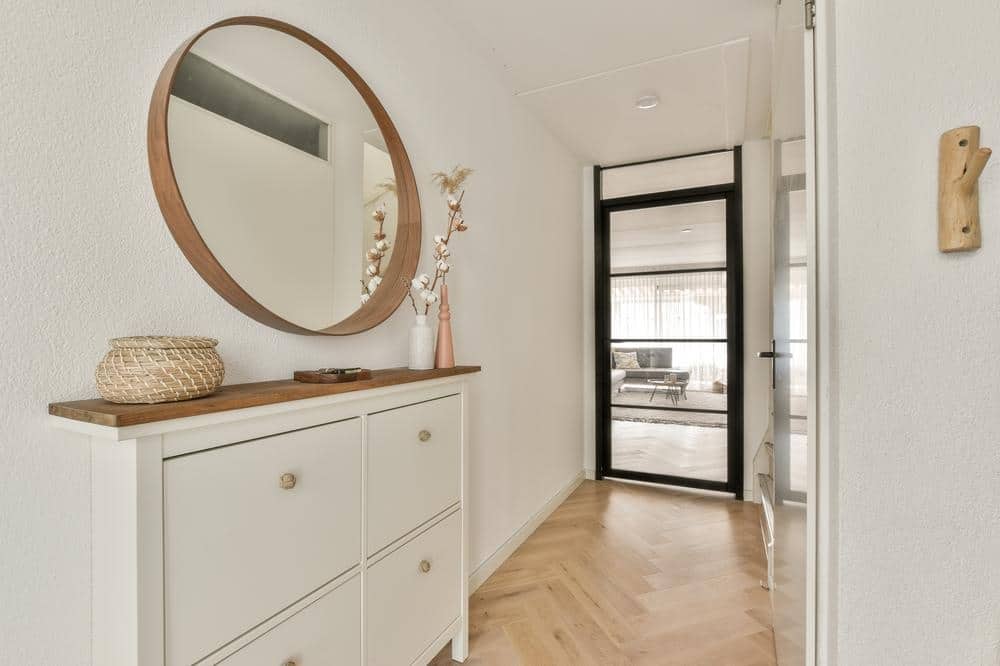White entryway hallway with a small closet with drawers and a round mirror on the wall