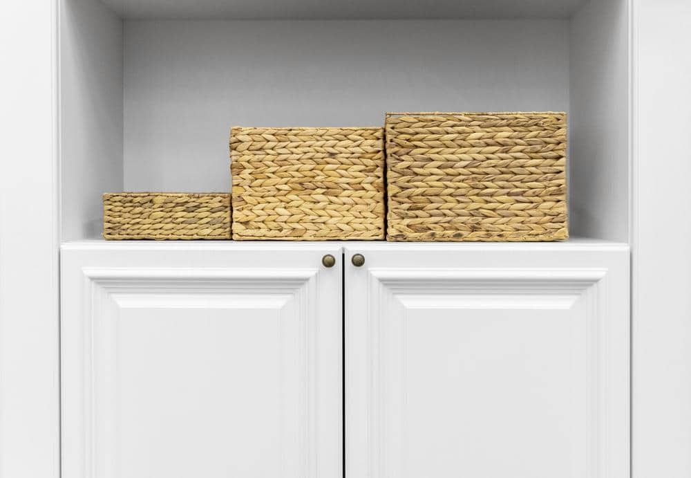 Three rattan storage baskets on a shelf aboce a closet