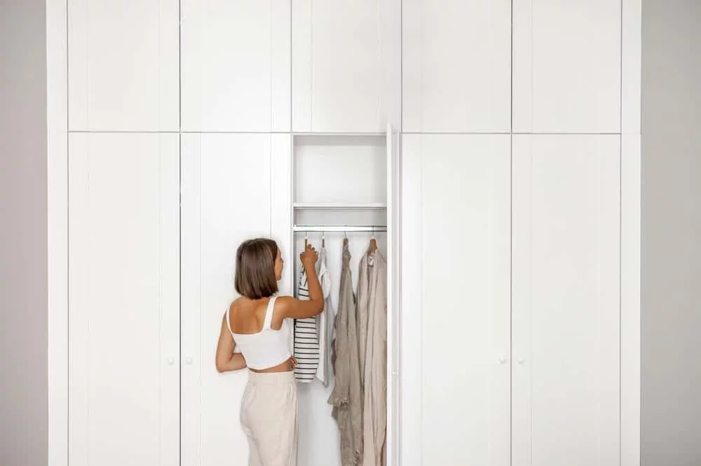 Mastering The Art of Organizing a Walk-In Closet: A Comprehensive Guide 1 A woman wearing white clothing standing in front of a white large closet with an open door